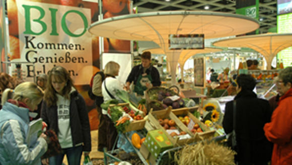Marktstand mit unterschiedlichen Obst- und Gemüsesorten, ringsherum Besucher der Grünen Woche.