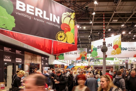 Eine Messehalle mit Ständen. In der Mitte der Fernsehturm aus Klemmbausteinen, links ein großes Banner mit der Aufschrift „Berlin“