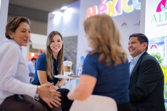 Four people sit around a table talking in a bright room with advertising boards in the background