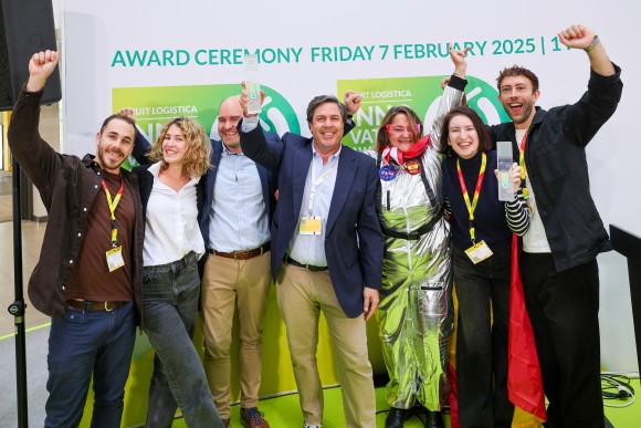 Group of eight people on stage at an awards ceremony, laughing as they hold up their trophies and celebrate their victory together.