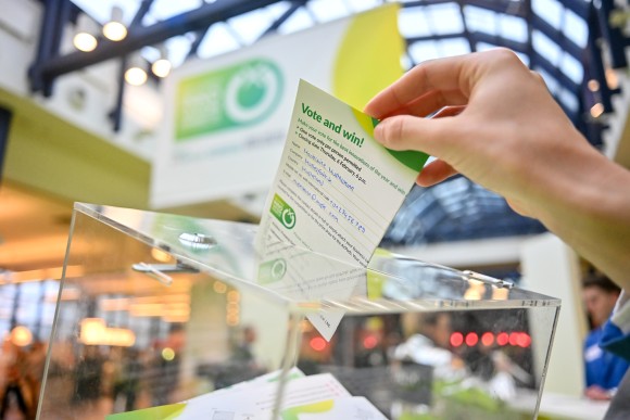 Eine Hand wirft eine ausgefüllte Stimmkarte in eine transparente Wahlbox.