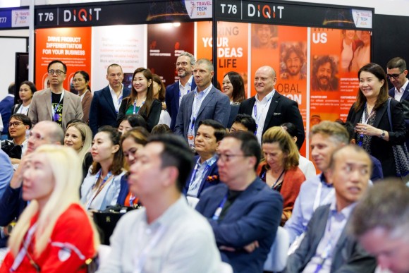 In a session at ITB Asia Conference, numerous visitors and delegates can be seen, either sitting and looking towards the stage. In the background, a travel-tech exhibitor's booth is visible.