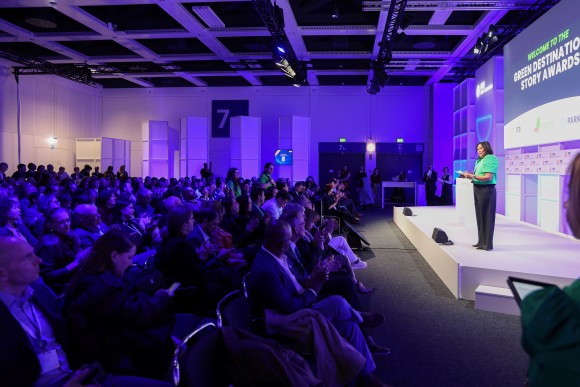 Eine Frau steht auf einer Bühne des ITB Berlin Kongress und spricht zu einem großen sitzenden Publikum in einem blau beleuchteten Saal.
