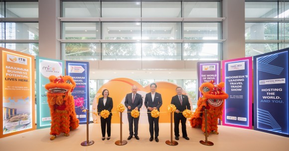 Alt Text: Four people cut a ribbon at the opening ceremony of ITB Asia 2025, with two lion dance performers standing on either side of them.